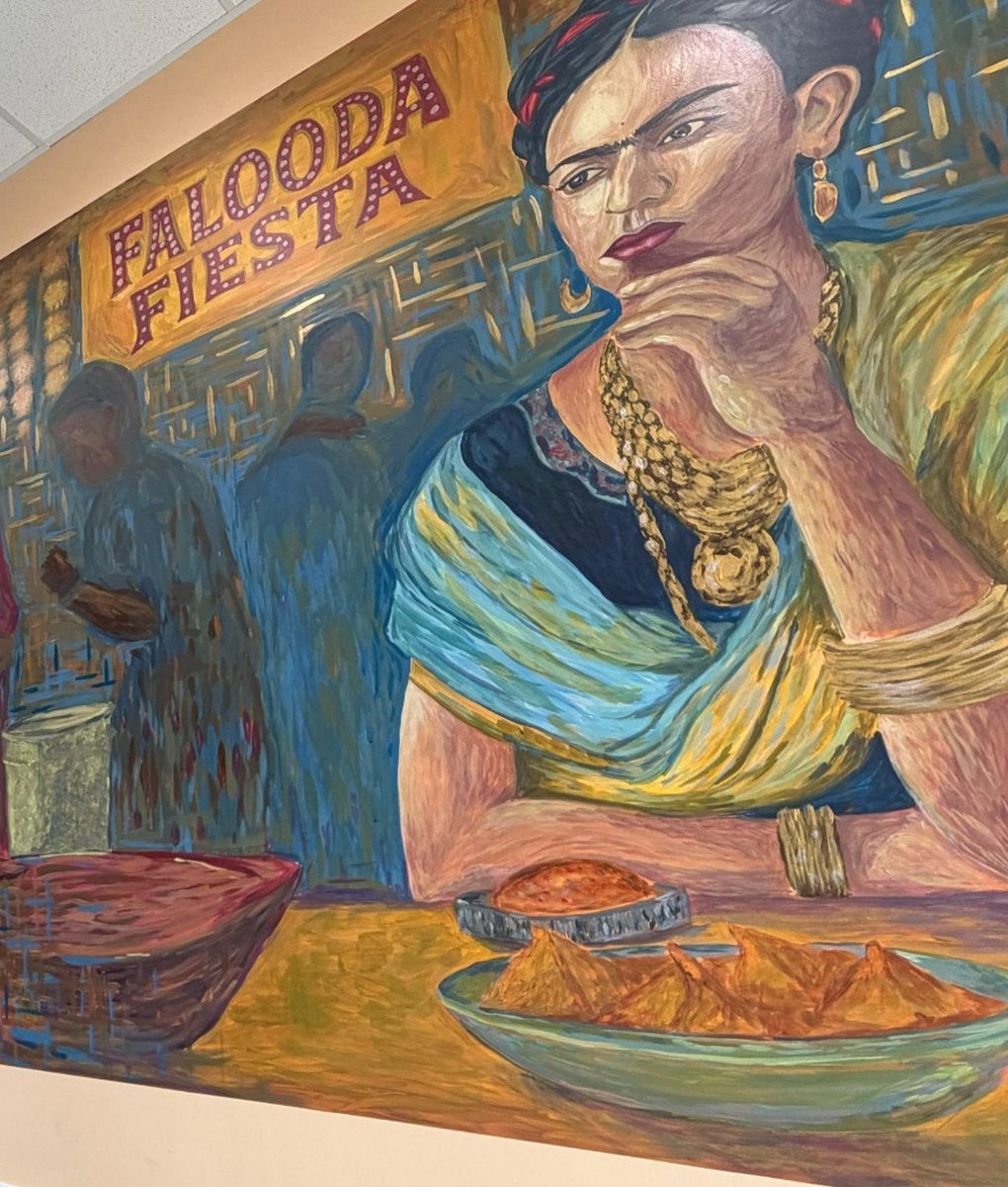 The hand-painted Falooda Fiesta wall mural: a Frida-Kahlo-inspired figure at a chaat counter with a bowl of samosas